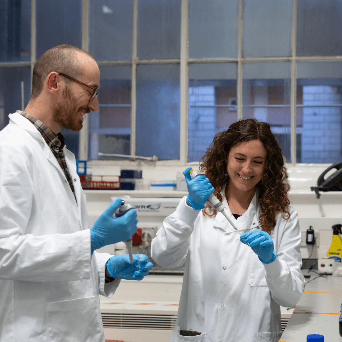 Two smiling scientists in a lab using pipettes.