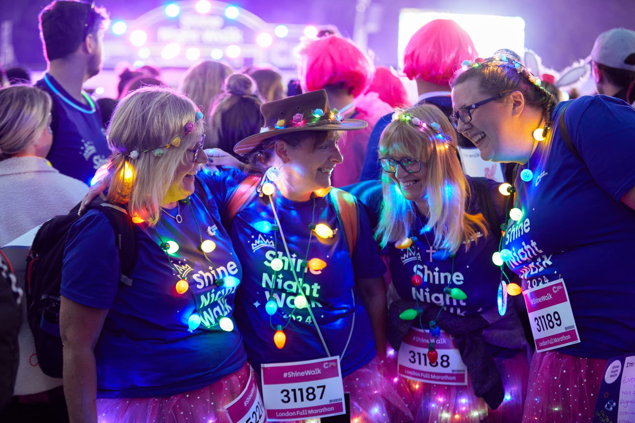 A group of 4 shine night walk participants lit up with fairy lights and smiling together.
