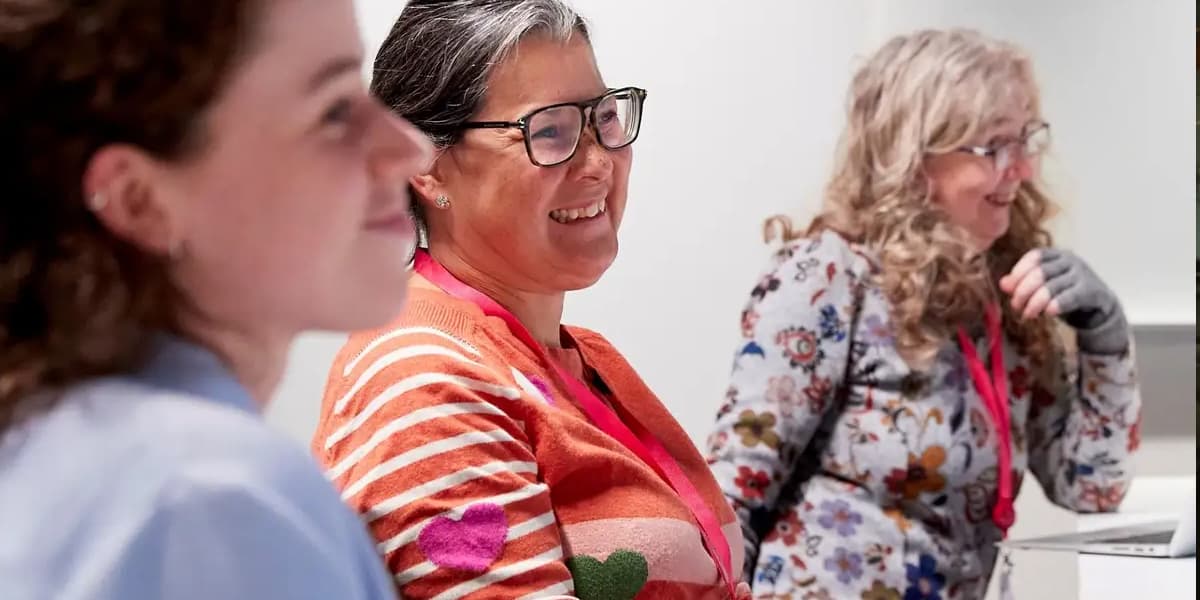 Three people sat at a table in a meeting. They are all smiling.