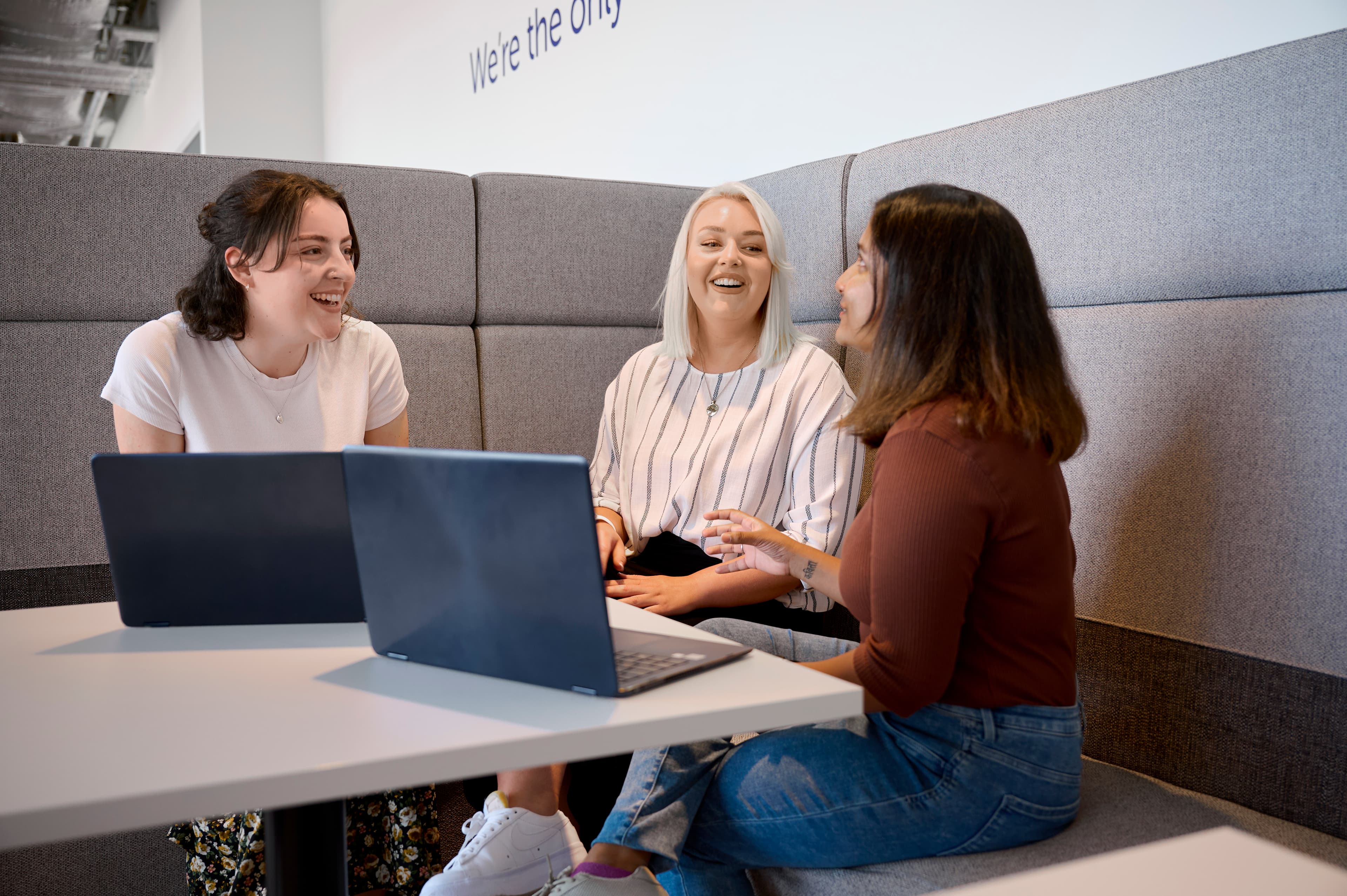 Photo of three member of Cancer Research UK staff sitting in a grey meeting booth having a conversation.
