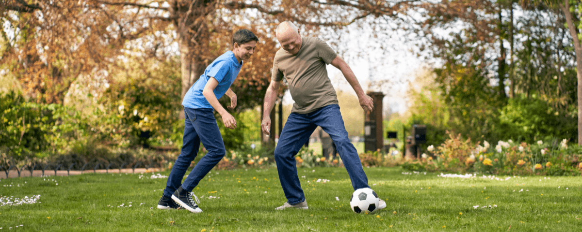 Man and young boy playing football together in a park.