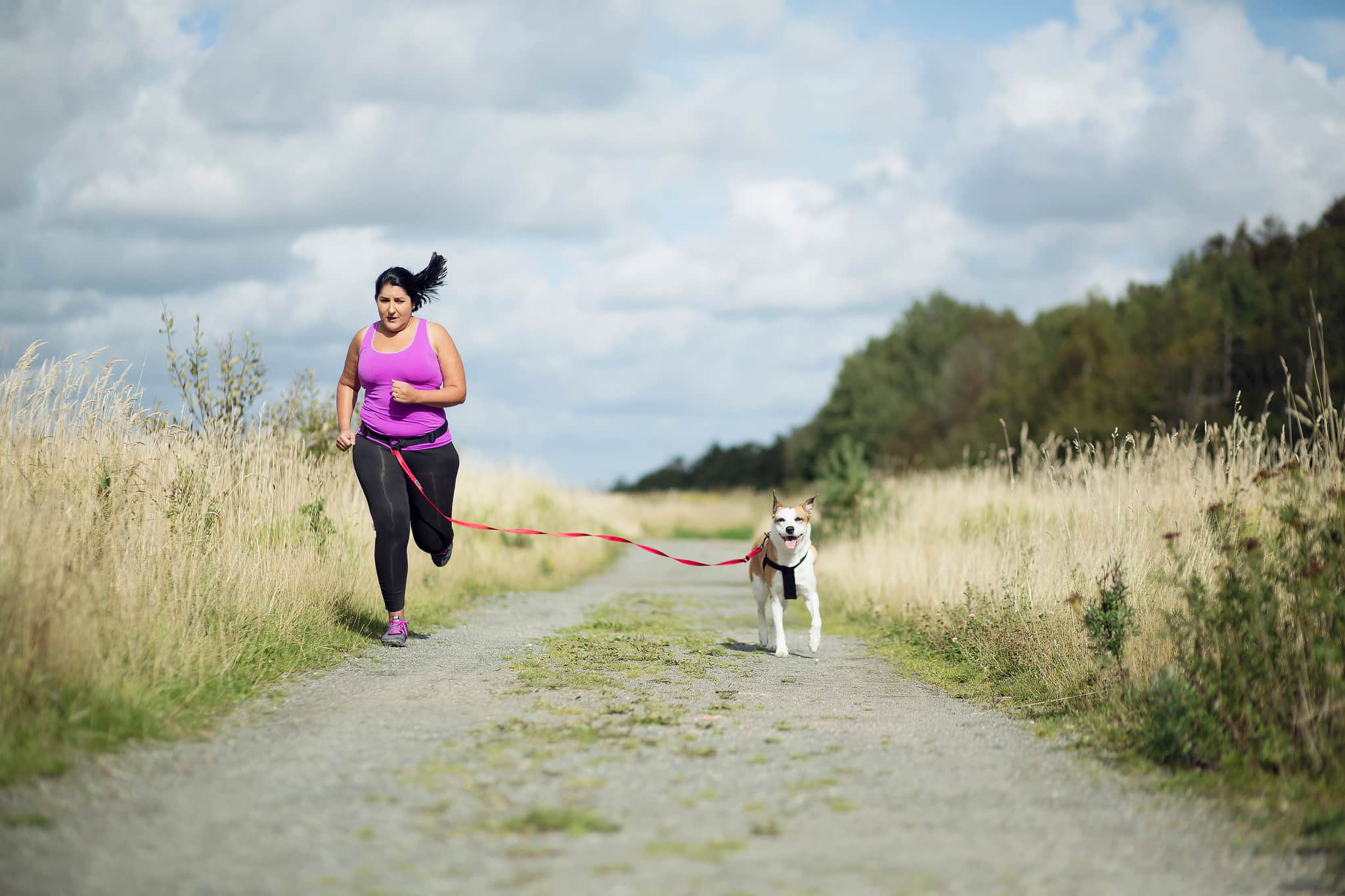A woman jogging with her dog along a grassy countryside.