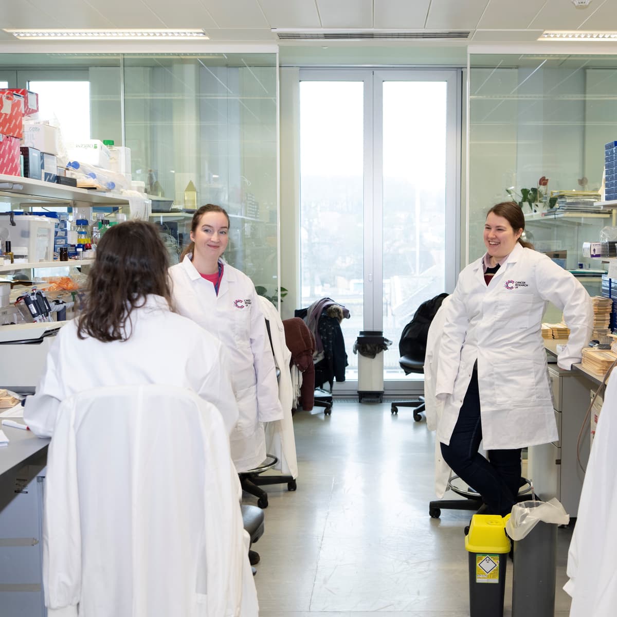 Three researchers stand talking in laboratory.