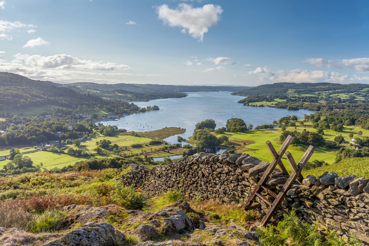 Landscape image of the Lake District on a sunny day. You can see fields, a lake and a few hills.