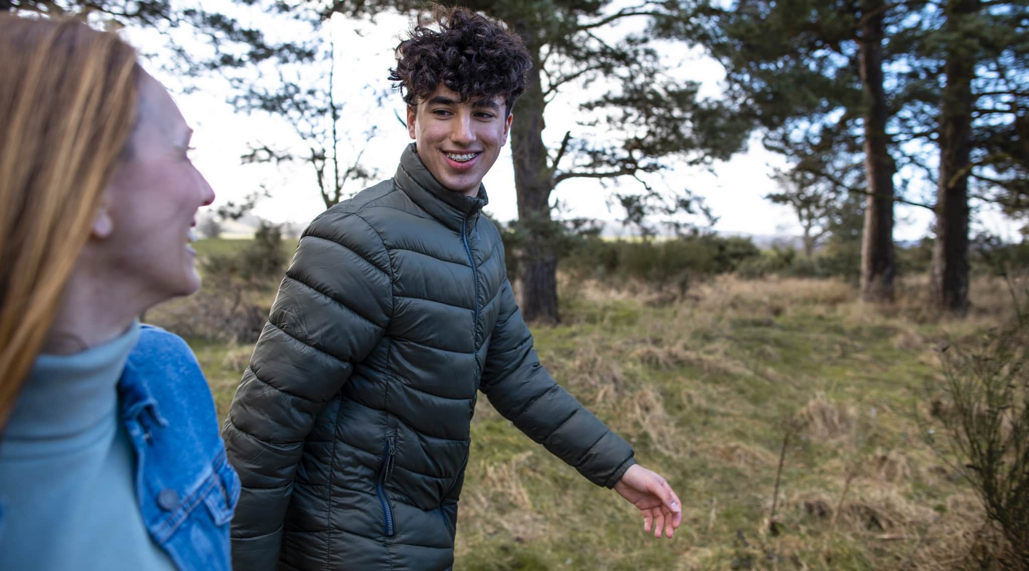 A man and woman smiling walking together through a grassy woodland path.