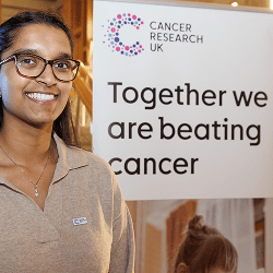 A photo of a Campaigns Ambassador in front of a sign that reads Together we are beating cancer.