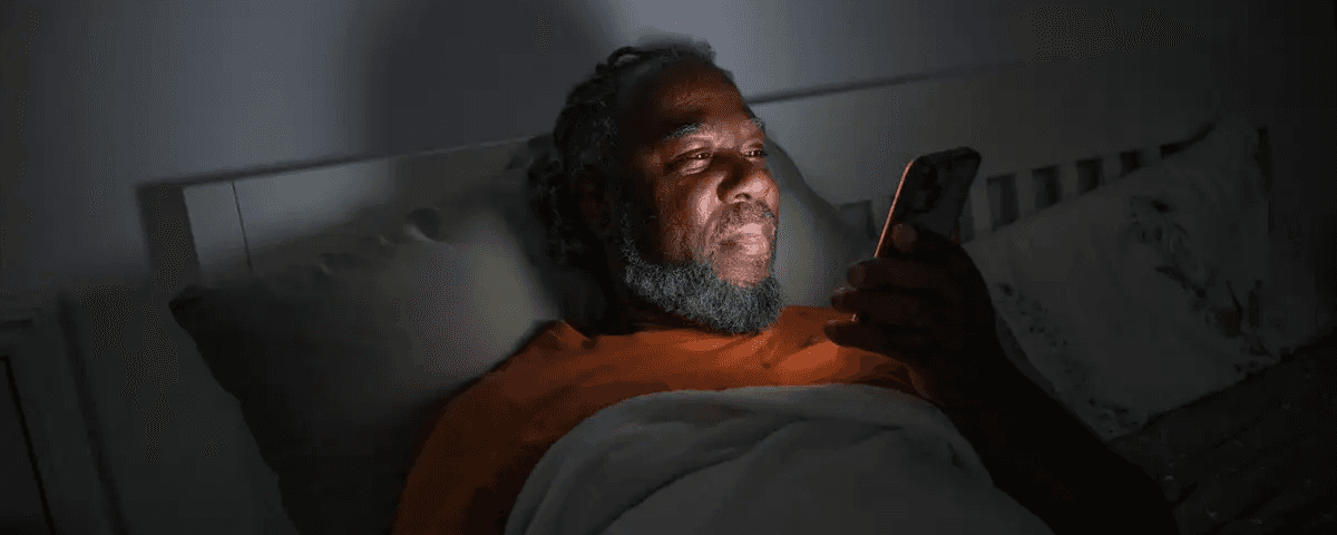 A man is in bed reading information on his phone.
