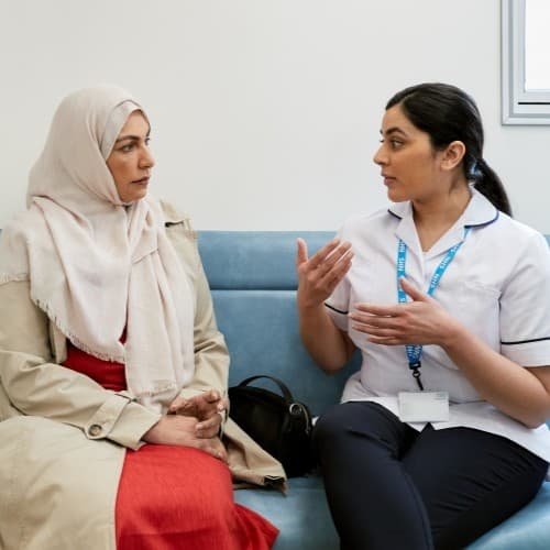 A healthcare professional is discussing treatment with a patient in a consultation room. They are both women.