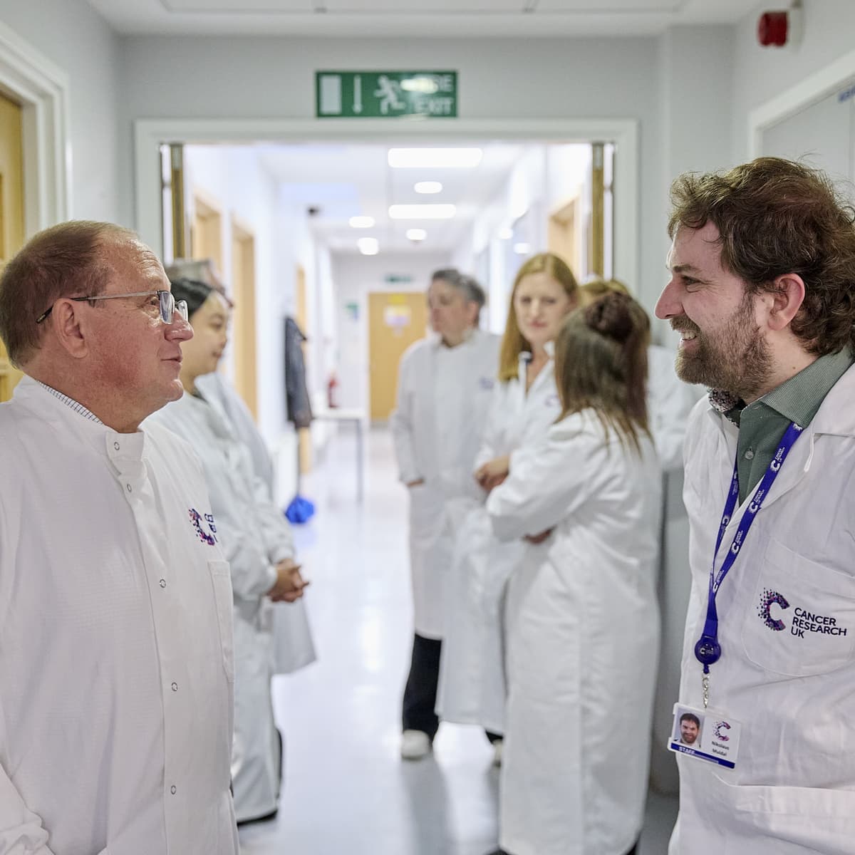 Several people stood in a hallway wearing labcoats.