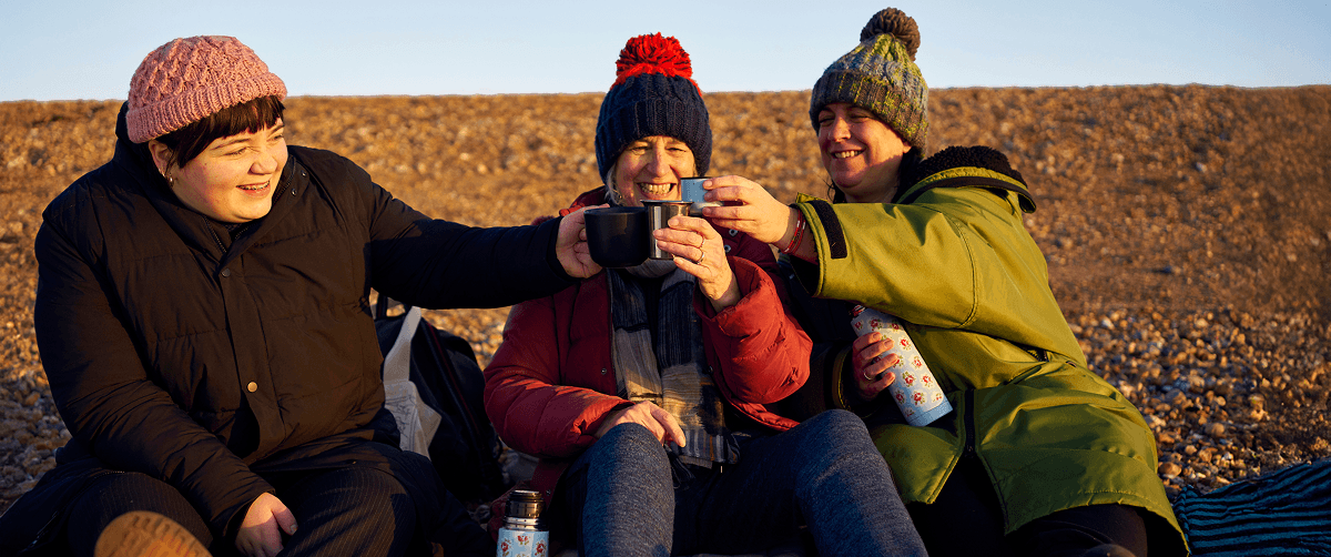 A photo of three people enjoying a hot drink outdoors.