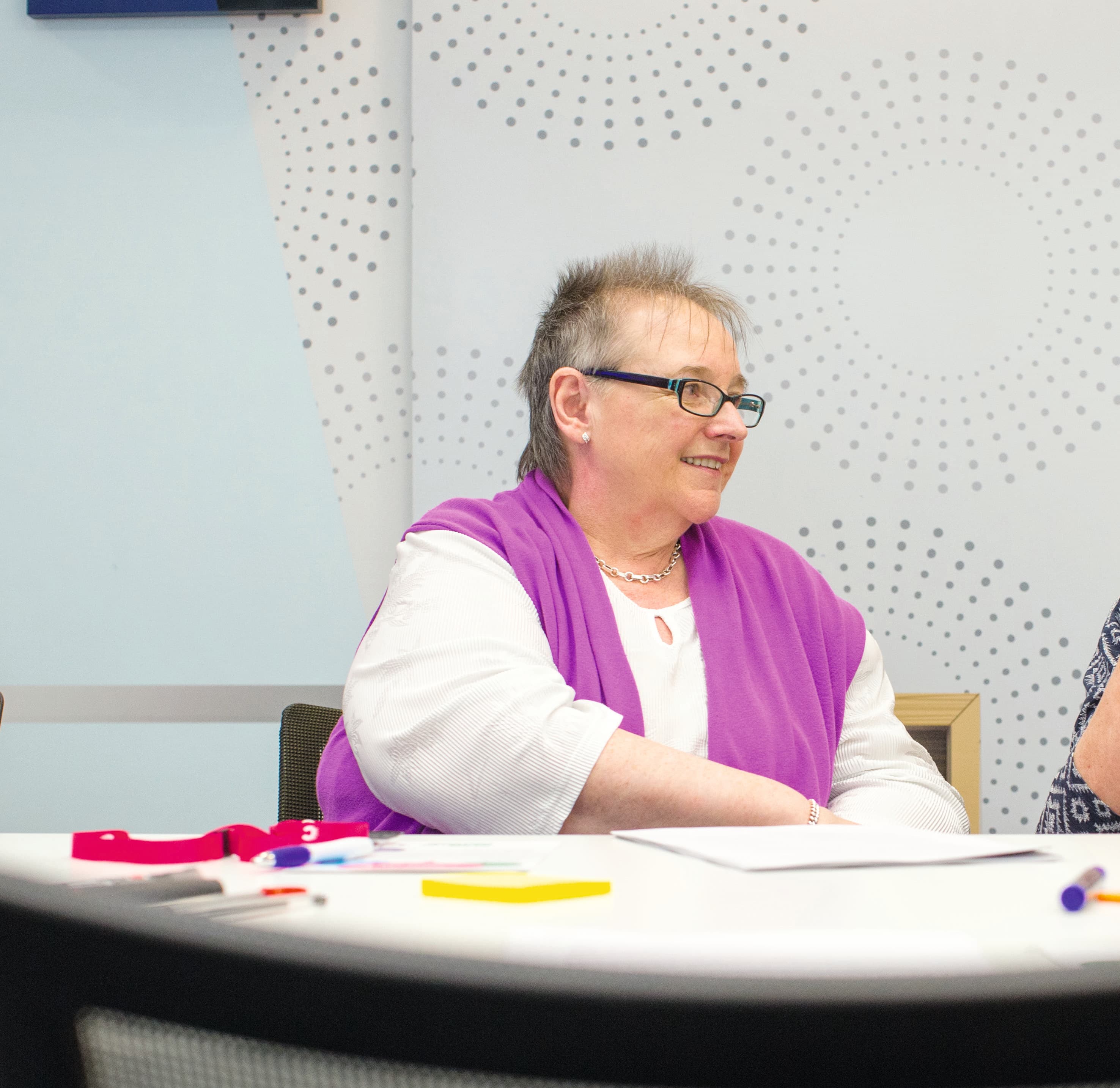 A picture of Margaret sitting at a table smiling.