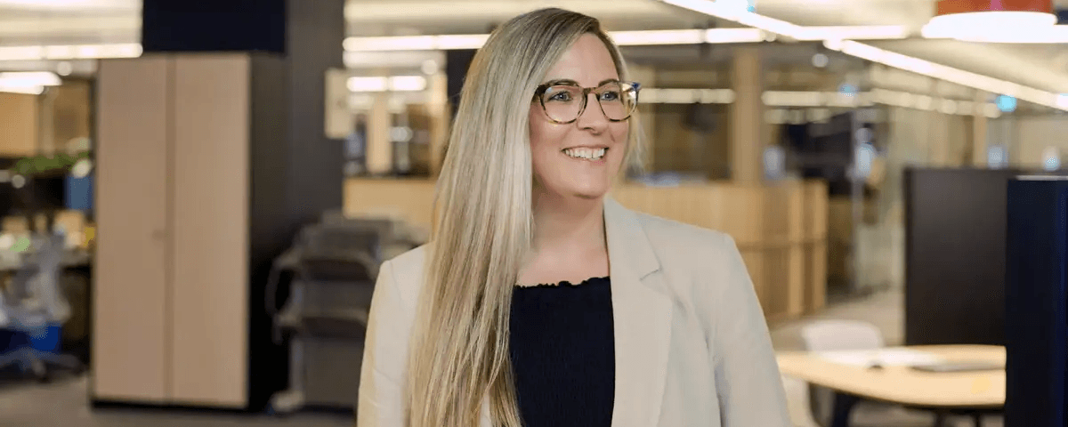 Image of female Cancer Research UK employee, standing and smiling in an office.