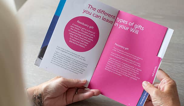 A woman holds a leaflet reading about how to leave a gift in her will.