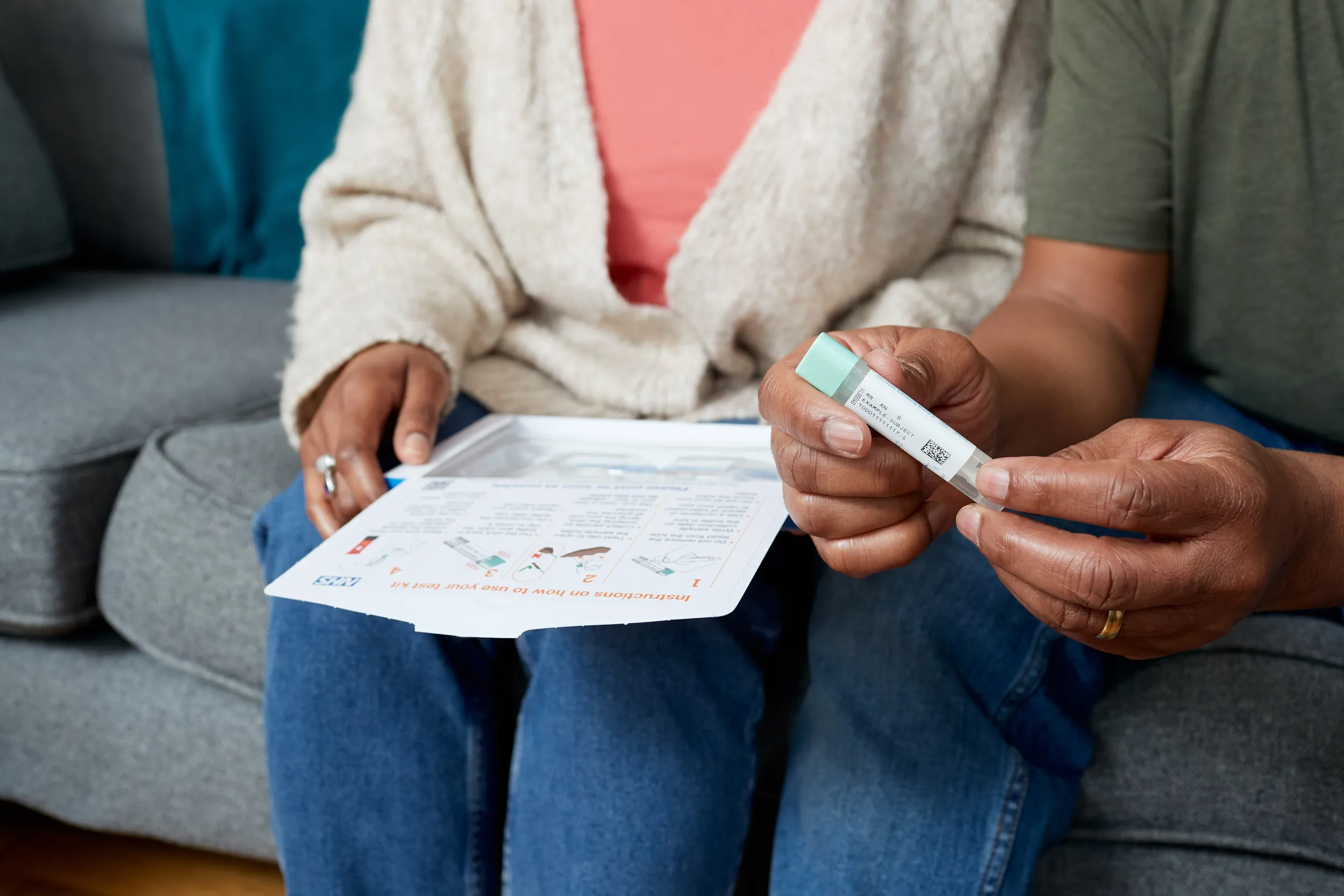Two people sitting next to each other on a sofa, holding a bowel screening test kit.