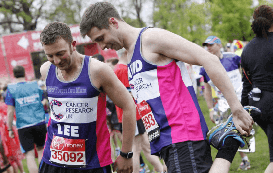 Two runners in CRUK vests stretching and looking down.