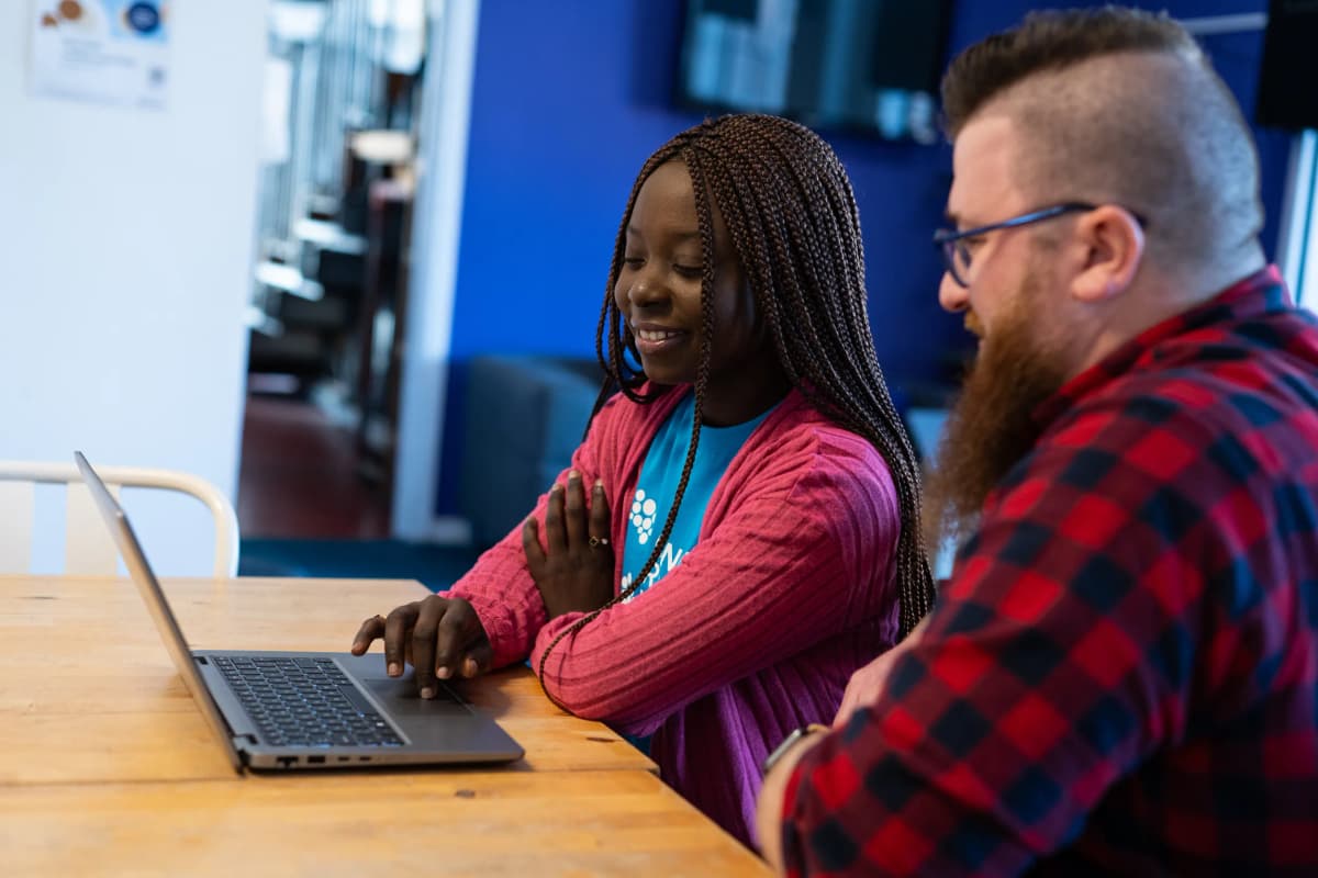 A man and woman sitting at a table and looking at a laptop.