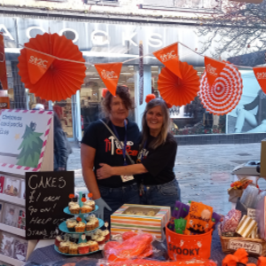 Two women in front of a Stand Up to Cancer stall set up in a shop