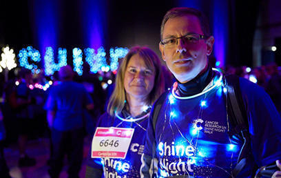 A man and a woman wearing Shine Night Walk t-shits and fairy lights around them