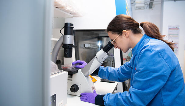 Female researcher in a lab looking down a microscope