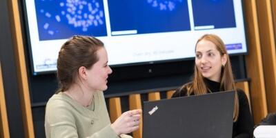 Two people sat at a table with a computer screen displaying a scientific image in the background