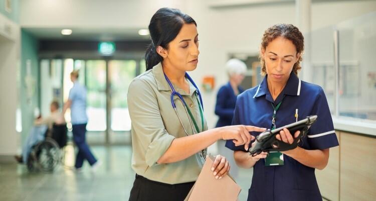 Two healthcare professionals in discussion in what appears to be a hospital corridor.