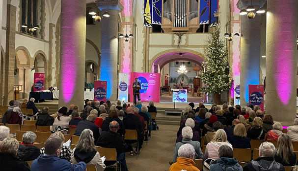 Supporters at an evening of Christmas music event, listen to the guest speaker explaining how gifts in Wills help fund research