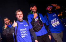 Four Shine night walk participants wearing glow in the dark necklaces and giving a thumbs up