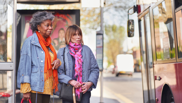 Two people stood at a bus stop, waiting to board.