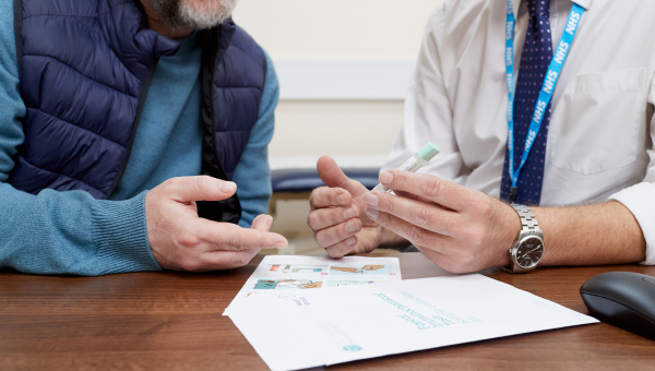 GP holding a FIT kit and leaflet towards a patient  GP holding a FIT kit and leaflet towards a patient