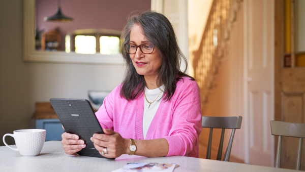 Woman sat at a table with a coffee reading information on a tablet device