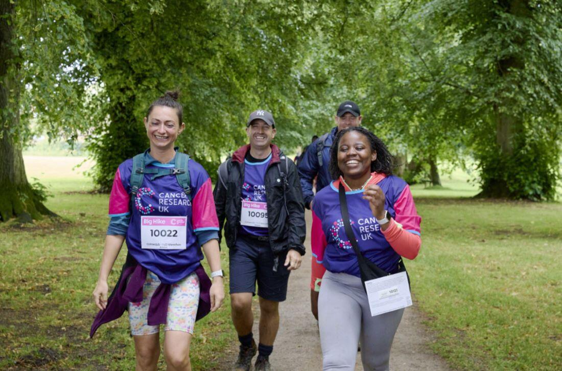 3 people laughing and smiling walking in the countryside wearing cancer research uk tshirts
