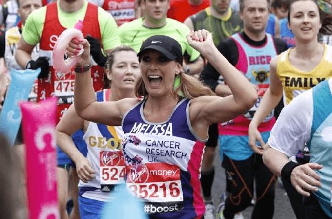 Take on the London Marathon Female runner wearing a CRUK running vest smiling holding her hands in the air during the London Marathon