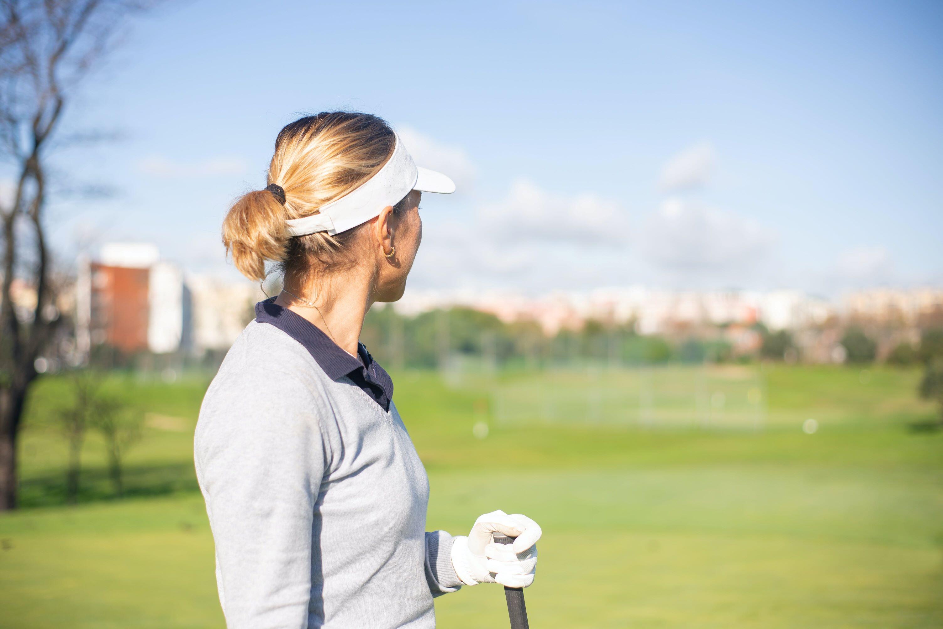 A picture of a women looking into the distance on a golf course wearing a golf hat