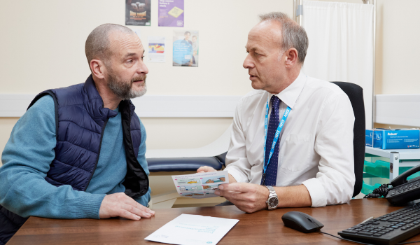 a GP talking to a male patient sat at a desk 