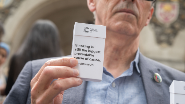 Man holding cigarette packet with statement on 'Smoking is still the biggest preventable cause of cancer'