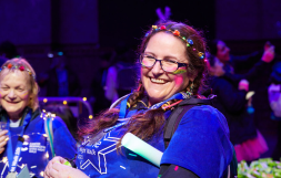 Smiling woman wearing a Shine Night Walk t-shirt and bright necklace and head band