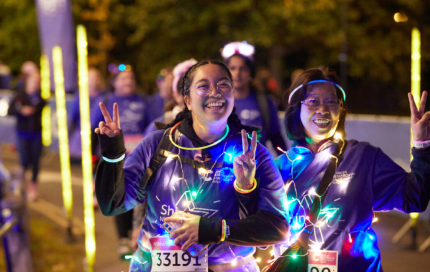 Two female shine participants wearing bright lights, smiling and doing the peace sign