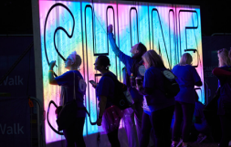 Image of people writing on a big, glow in the dark, Shine Night Walk sign