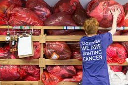 A stock processing volunteer with bags of donated items in a Cancer Research UK charity shop