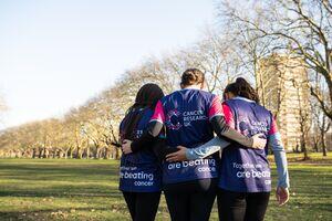 Three people showing off the backs of their Cancer Research UK t-shirts hugging eachother
