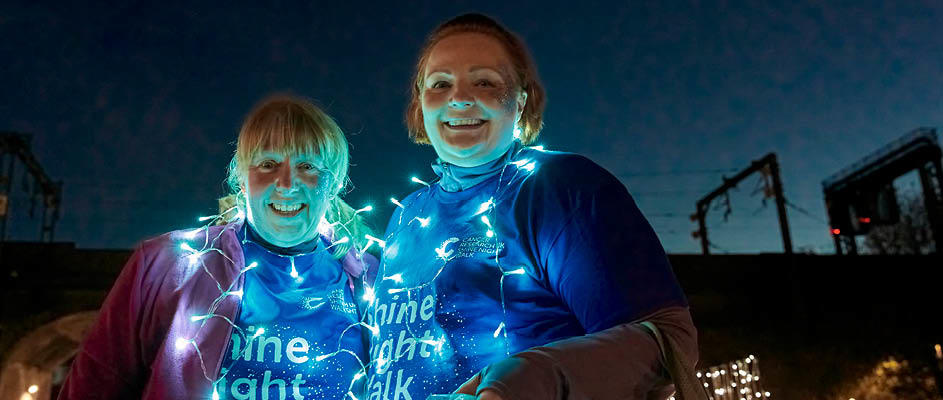 Strava Shine image Two women smiling at the camera with fairy lights across them at Shine Night Walk