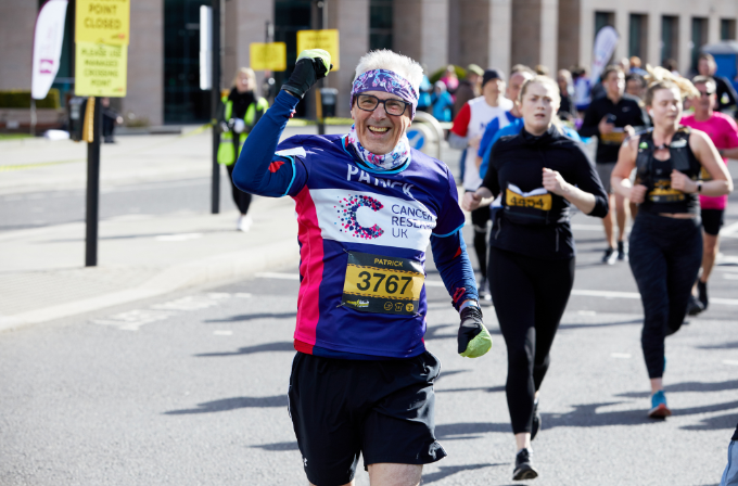 A man running the London Landmarks Half Marathon, he is wearing glasses, a purple bandana and he is smiling.