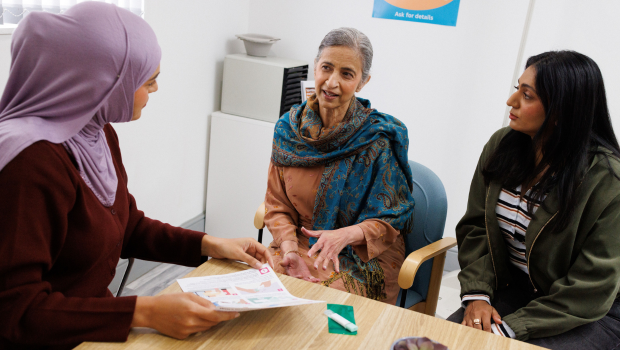 Female Dr sat at a desk showing a leaflet to two woman Female Dr sat at a desk showing a leaflet to two woman